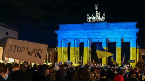 Das Brandenburger Tor in Berlin angestrahlt in blau-gelb während einer Protestkundgebung mit vielen Menschen davor