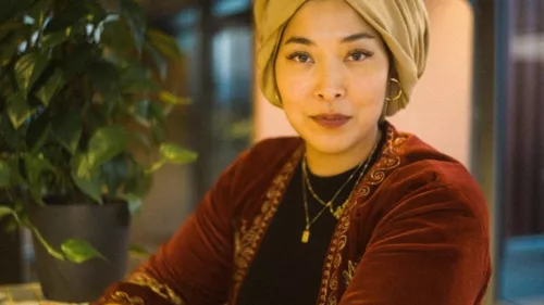 Esra trägt eine rote Samtjacke und ein goldfarbenes Kopftuch
