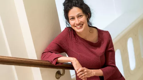 Payal Arora trägt ein dunkelrotes Kleid und lächelt in die Kamera. Sie steht in einem Treppenhaus.