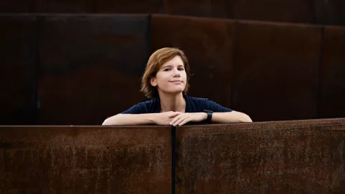 Ingrid Brodnig sitzt zwischen Stuhlreihen und stützt die Unterarme auf die Lehnen. 