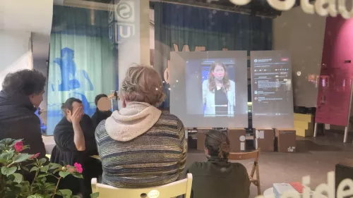 Menschen sitzen beim Public TikTok Viewing im Halbkreis um eine Leinwand, auf der TikTok Videos mit zugehörigen Kommentaren zu sehensind.