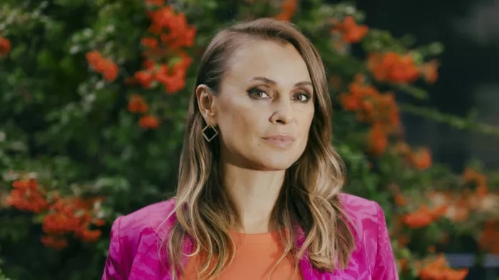 Jagoda trägt einen Blazer mit Leopardenmuster, offene Haare und Ohrringe. Sie steht vor einem blühenden Busch.