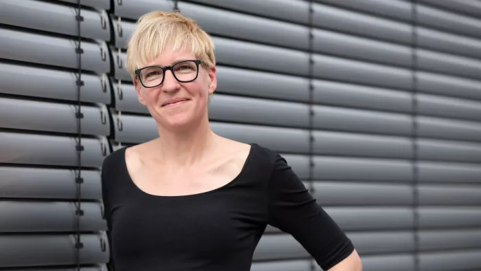 Dies ist ein Bild von Eva Wolfangel. Sie trägt eine Brille, kurze Haare und steht vor einer Jalousie.