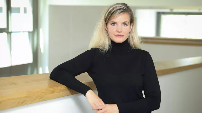 Johanna Degen trägt einen Rollkragenpullover, lange offene Haare und stützt ihren Unterarm auf ein Geländer.