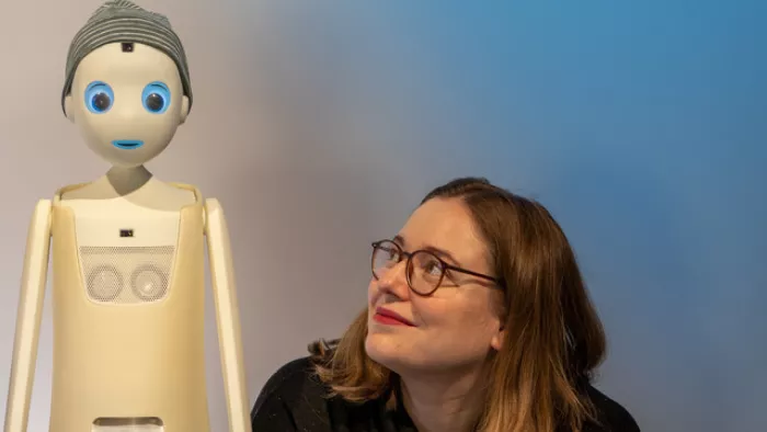 Katharina neben einem humanoiden Roboter mit Mütze.