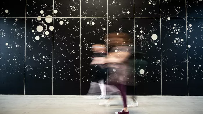 Kunstinstallation – viele helle Punkte auf einer Wand, davor Menschen