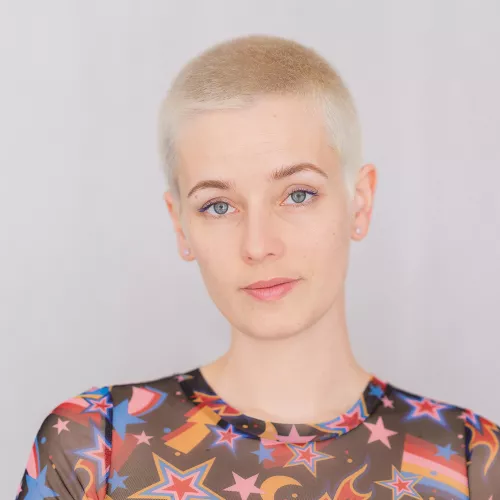 Selbst-Portrait von Laura Zalenga in buntem Shirt vor hellgrauem Hintergrund.