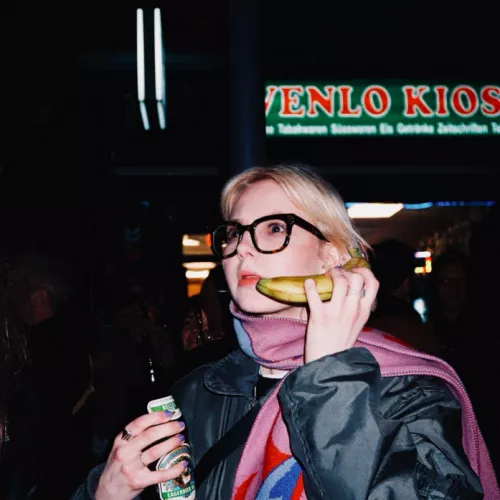 Foto einer jungen Frau, die eine Banane an ihr Ohr hält