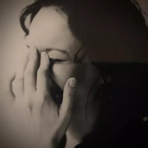 Das Bild zeigt eine lockige weiblich zu lesende Person, die eine Hand vor ihr Gesicht hält