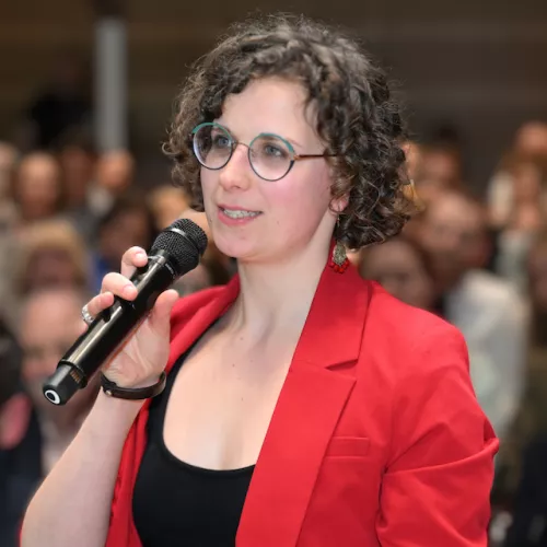 Junge Frau mit rotem Blazer, die in ein Handmikro spricht. 