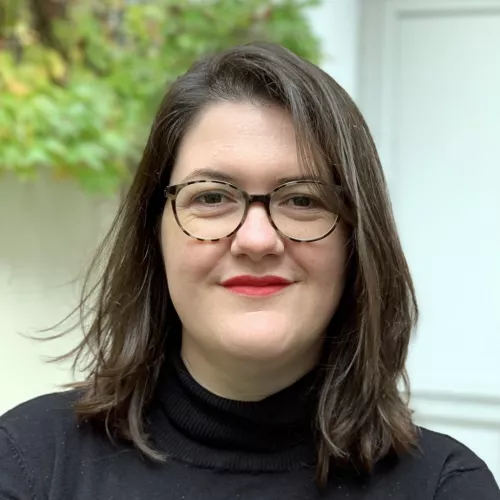 Portrait of a person with brown hair, glasses and red lipstick wearing a black turtle neck.