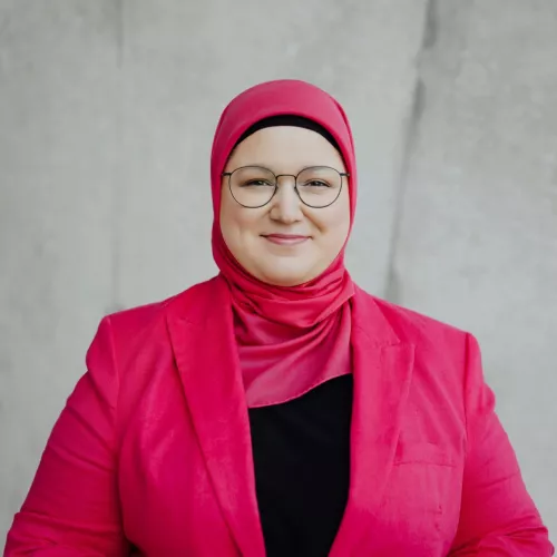 Frontalfoto von Zehra Öztürk vor Betonwand mit pinkem Kopftuch und pinker Jacke