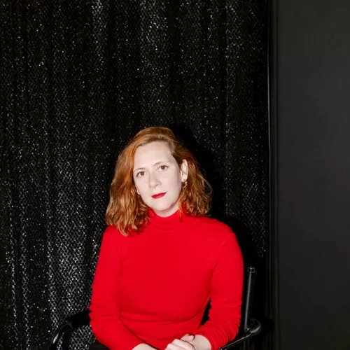 rothaarige Frau in rotem Pullover vor Glitzervorhang. 