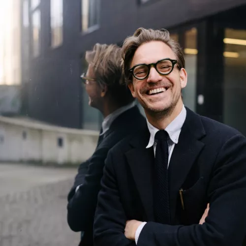 Der Sprecher im Anzug und mit verschränkten Armen. Er trägt eine Brille und lächelt.