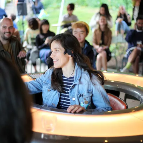 Timna is sitting in a doughnut shaped table hosting a Talkaoke session.