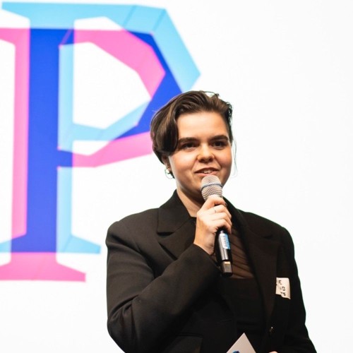 Marie standing with a microphone in front of a large pink and blue P which is the Prototype Fund logo