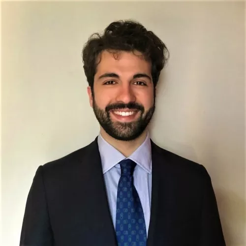 Alessandro wearing a blue suit and a light blue tie, smiling