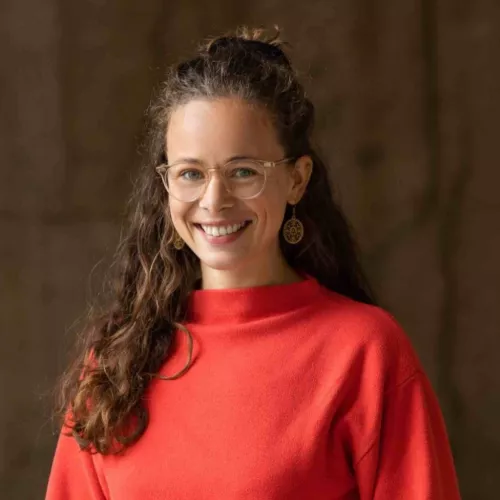 The speaker is dressed in a red jumper and has long, curly hair.