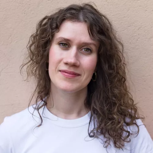 Anna-Mira Brandau steht vor einer Mauer und lächelt in die Kamera. 