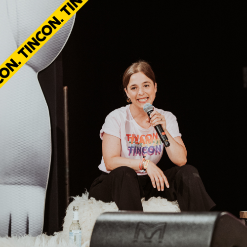 Carla Barzen sitzt auf einem Hocker auf einer TINCON Bühne und spricht in ein Mikrofon.