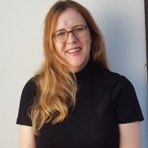 Christiane hat lange rotblonde Haare und lächelt freundlich in die Kamera. Sie trägt Brille und auf ihrer Stirn hat sie ein rötliches Feuermal.