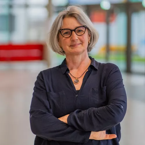Frau mit grauen, mittellangen Haaren, hornfarbener Brille und dunkelblauer Bluse