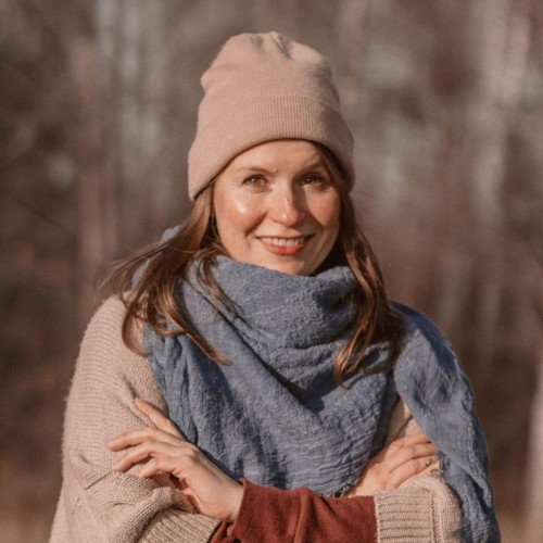Torso-Porträt von Caroline Helbing, in Strickponcho, Schaltuch und Mütze im Sonnenschein von Herbstwald