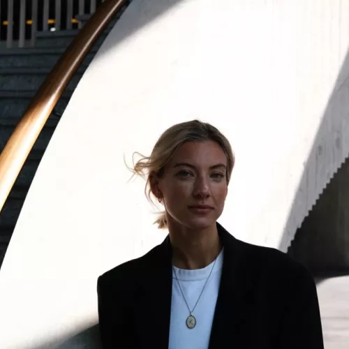 eine blonde person steht vor einer grauen treppe. 