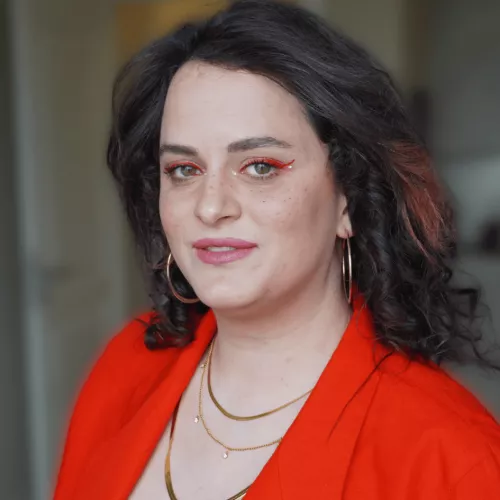 Eine Frau trägt einen roten Blazer und drei dünne goldene Ketten.