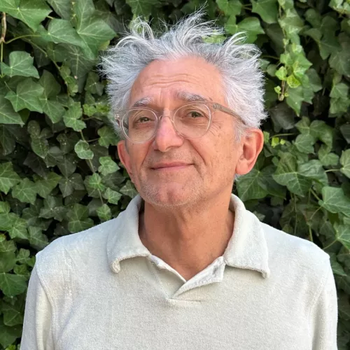Auf dem Portrait ist Francis Gay zu sehen. Er trägt eine durchsichtige Brille und schaut ein wenig seitlich geneigt in die Kamera. Er trägt ein helles T-Shirt mit Kragen. 