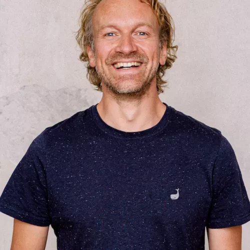 Fridtjof lacht in die Kamera. Er hat ein blaues Shirt an und blonde Haare sowie einen Bart