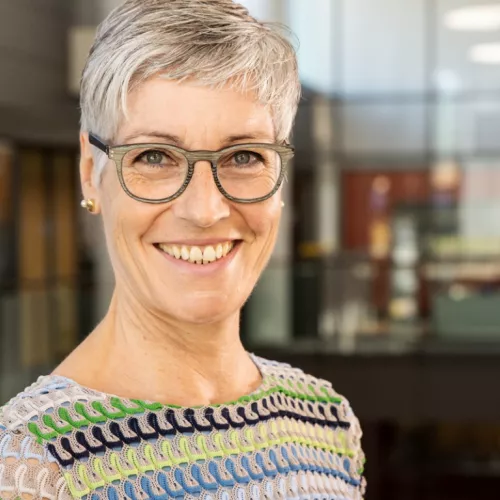 Frauenkopf mit kurzen weißen Haaren und Brille, sie lacht