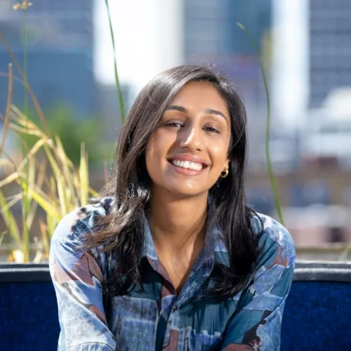Image of a brown woman with dark hair, wearing a blue shirt. Background is of a cityscape 
