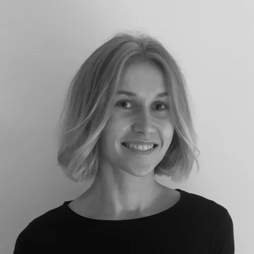 portrait photo in black and white of a young blonde woman with open chin-length hair, smiling slightly sideways into the camera in a friendly manner