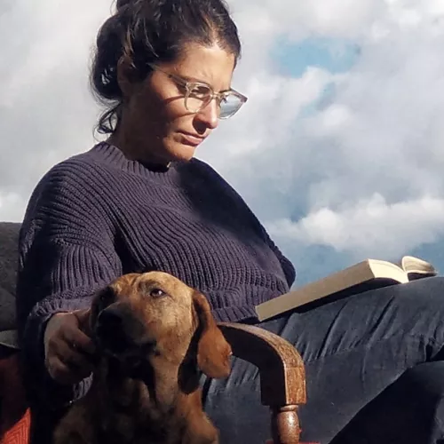 Eine Frau mit Brille liest ein Buch. Vor ihr ist ein Hund