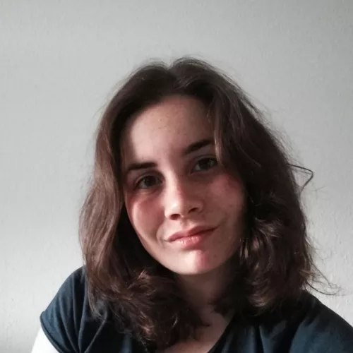 Ein Bild von mir. Ich habe braune, mittellange Haare, trage ein dunkelblaues Shirt und lächle direkt in die Kamera. Den Kopf halte ich leicht schräg.