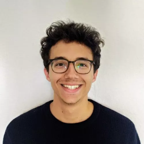 Ein Porträtfoto eines lächelnden Mannes mit braunen Haaren und braunen Augen.