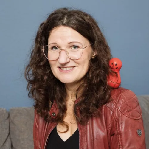 Profilbild Frau mit langen Haaren und Brille mit roter Figur auf der Schulter