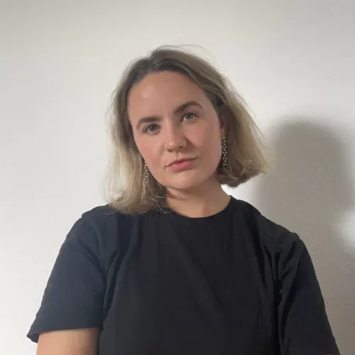Eine Person mit kurzen blonden Haaren vor weißem Hintergrund