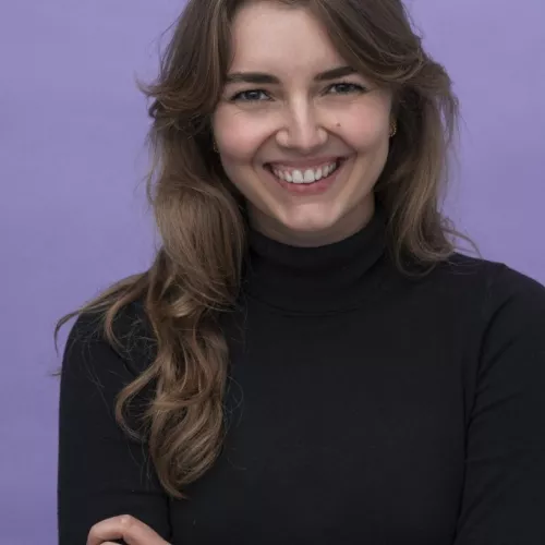 Frau (Luisa Houben) mit langen blonden Haaren und schwarzem T-shirt vor lila Hintergrund