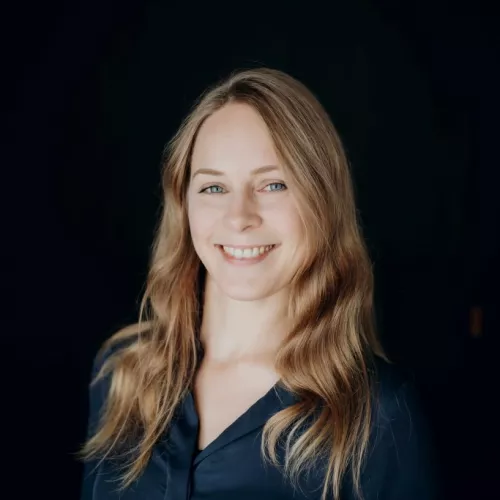 Profilbild von einer Frau mit blonden Haaren und dunkelblauer Bluse.