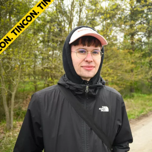 Jakob Springfeld lächelt in die Kamera. Er trägt eine schwarze Regenjacke mit Kapuze auf. Im Hintergrund sind Bäume zu sehen.