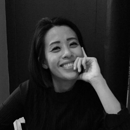 Black and white portrait image of a Chinese person smiling with her hands propping up her chin