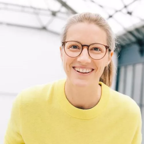 Lisa Zauner, in gelbem Pullover, lacht und schaut in die Kamera