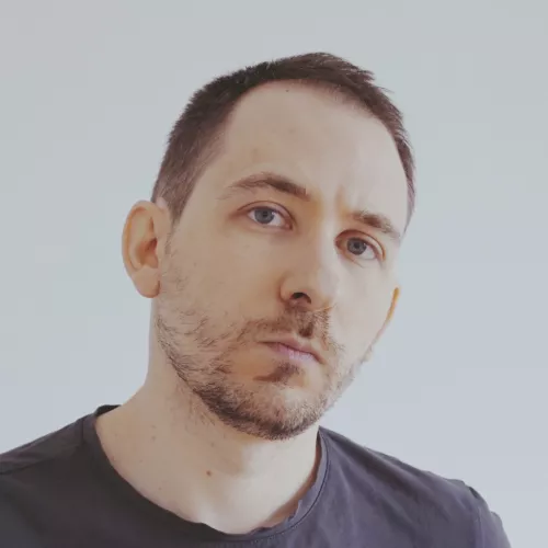 A picture of a white man with short hair, wearing a grey t-shirt.