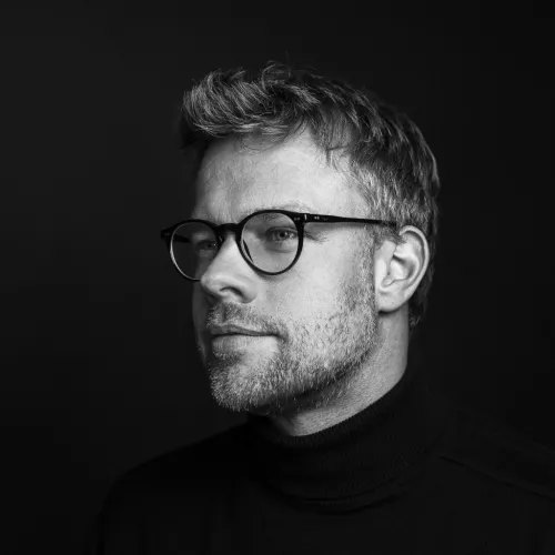 Mann mit Brille und drei-Tage-Bart, der von der linken Seite fotografiert worden ist