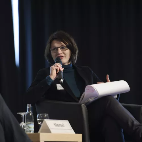 Miriam Menzel sitzt bei einem Podium auf einer Bühne und spricht in ein Mikrofon.