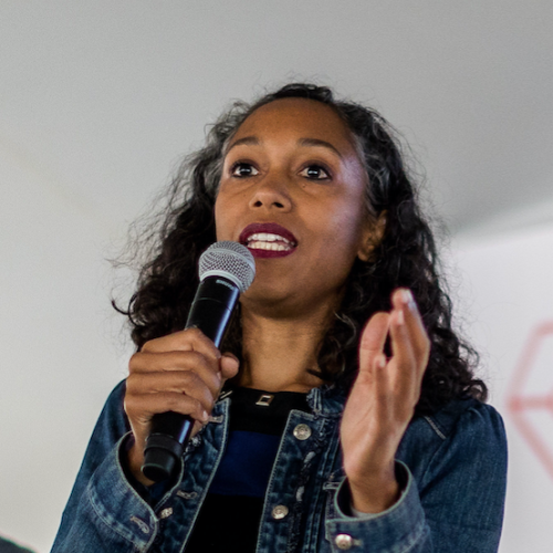 Brown Skinned Woman with dark hair speaking into a mic