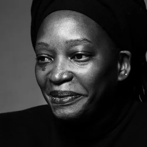 Monochrome portrait photo of a smiling black woman wearing a black headscarf and a black turtleneck.