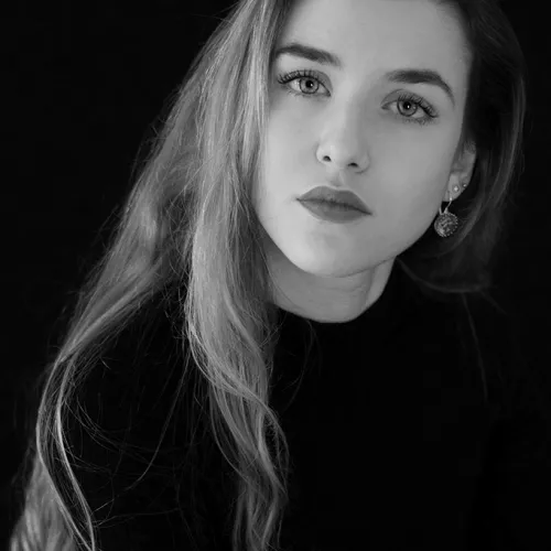 A black and white photograph of a young woman, with an oval face, bright eyes, and long blonde hair. She's wearing a black turtleneck and earrings.